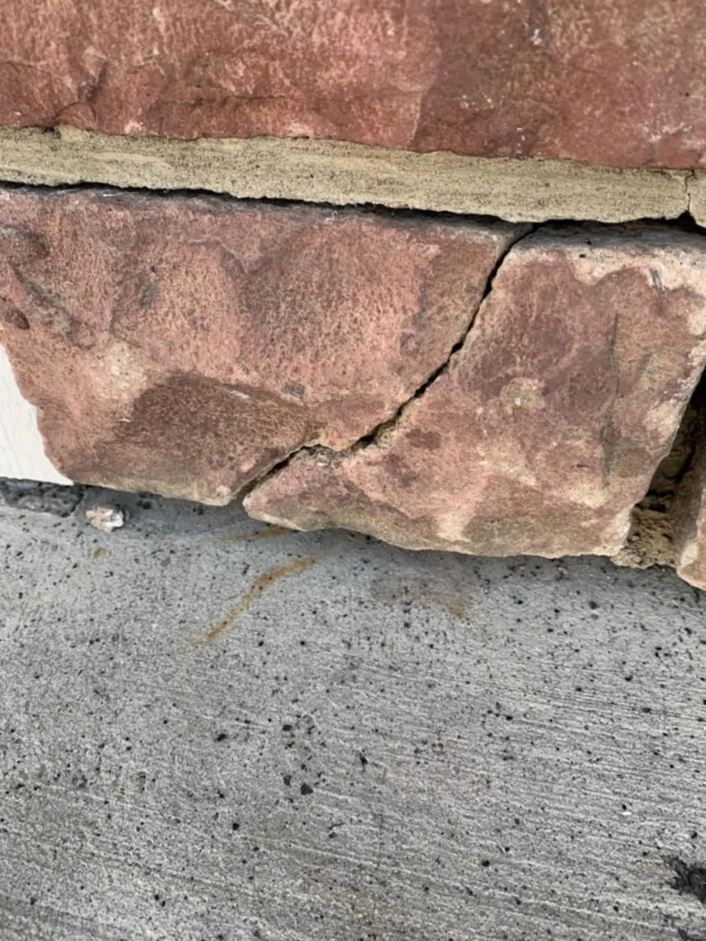 Snow and impact damaged manufactured stone on a Calgary garage exterior