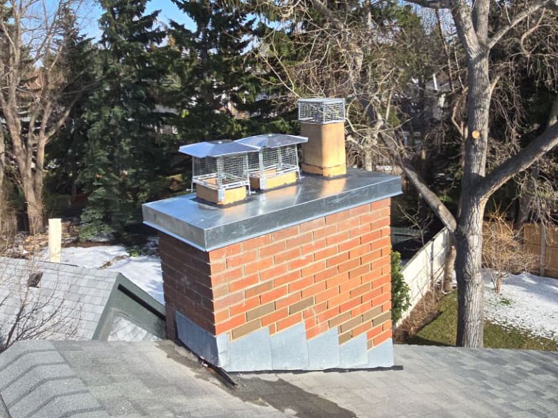 Completed brick chimney repair with a new custom metal chase cap and chimney caps in Calgary.