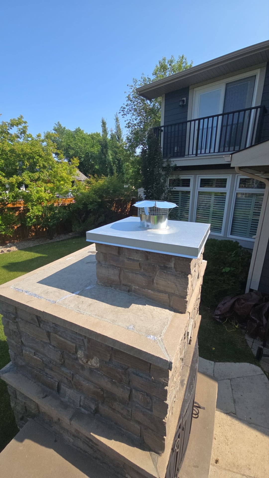 Custom white metal chimney cap installed on a stone masonry chimney in Calgary.