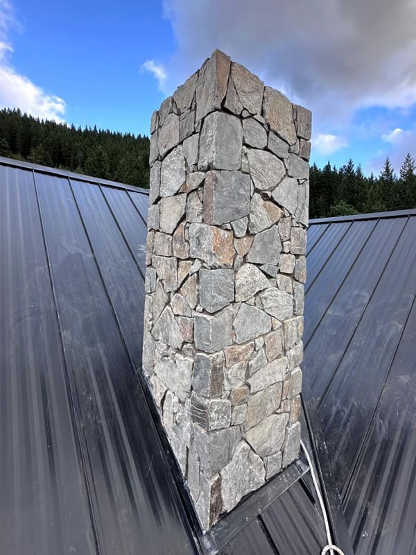 Custom natural stone chimney installed on a metal roof in Alberta